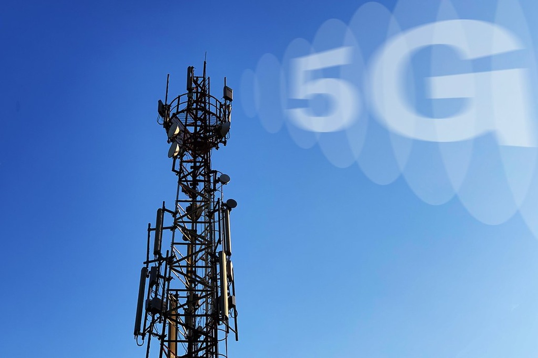 Telekommunikationstorn med 5G-antenner mot en blå himmel.